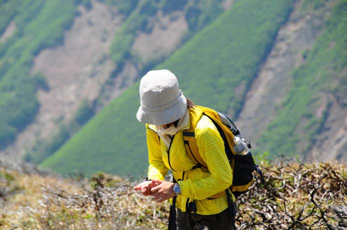 アウトドアの帽子をかぶって登山中の女性