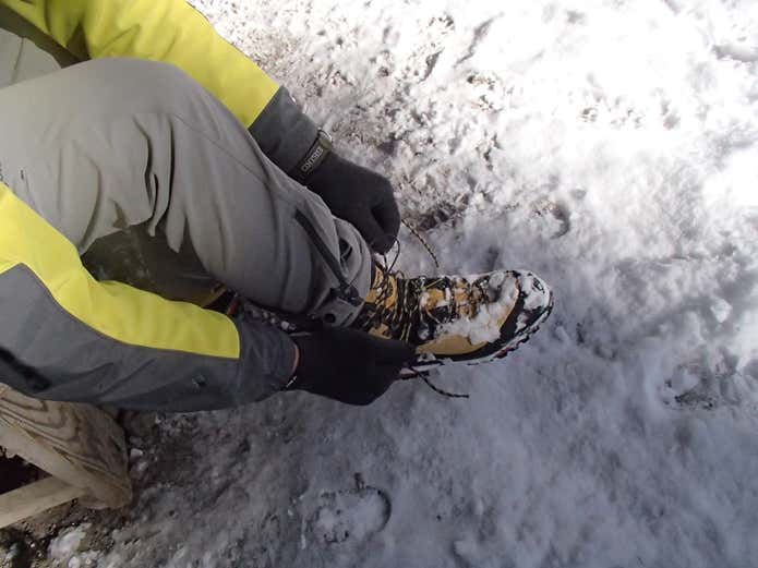雪山で登山靴の紐を直す登山者