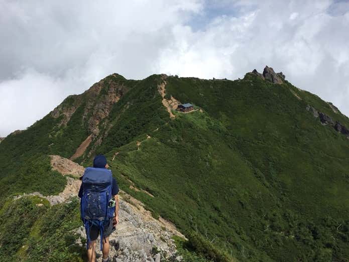 青いウエアとザックで登山を楽しむ人