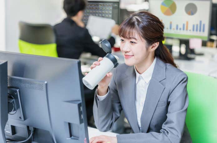 デスクで水筒のコーヒーを飲む会社員