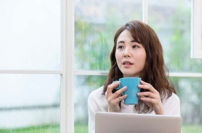 雨の日の窓際でパソコンの前に座っている女性