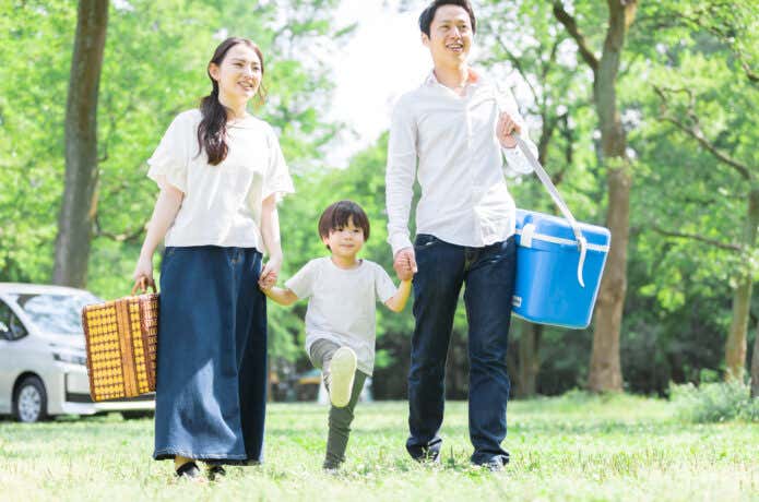 クーラーボックスを持ってキャンプ場に向かう家族