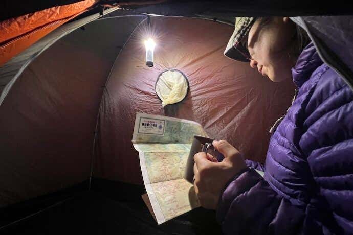 テント内でランタンの明かりの元、地図を読む