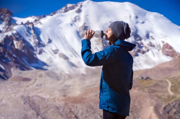 登山中にスクイズボトルで水分補給する女性