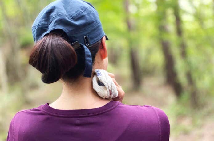登山中にかいた汗を拭いている、帽子を被った女性