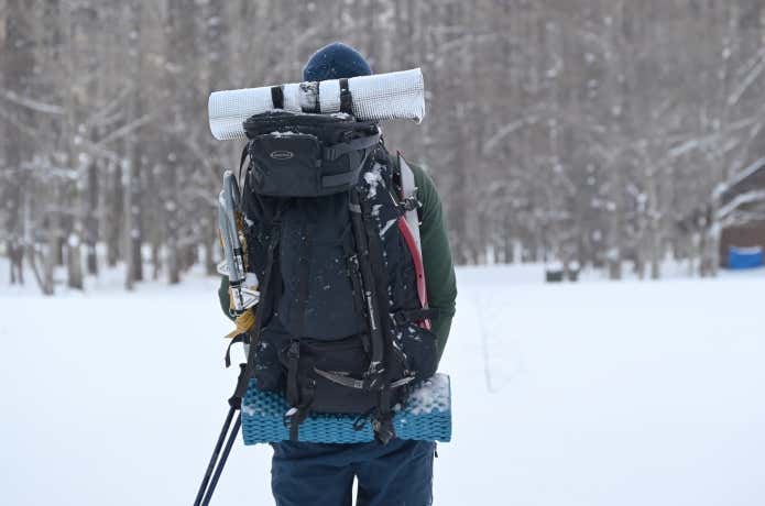 雪山のテント泊装備を背負う人