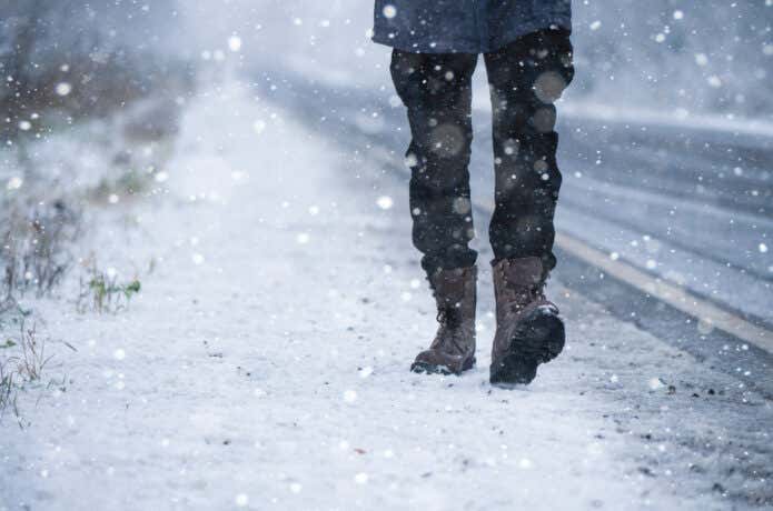 防寒ブーツを履いて雪の降る道を歩く人