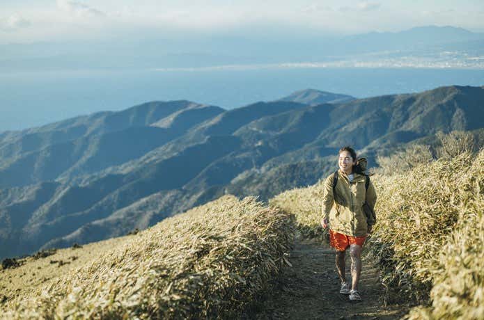 Tevaのサンダルを履いて、山と海をバックに高原を笑顔で歩く女性