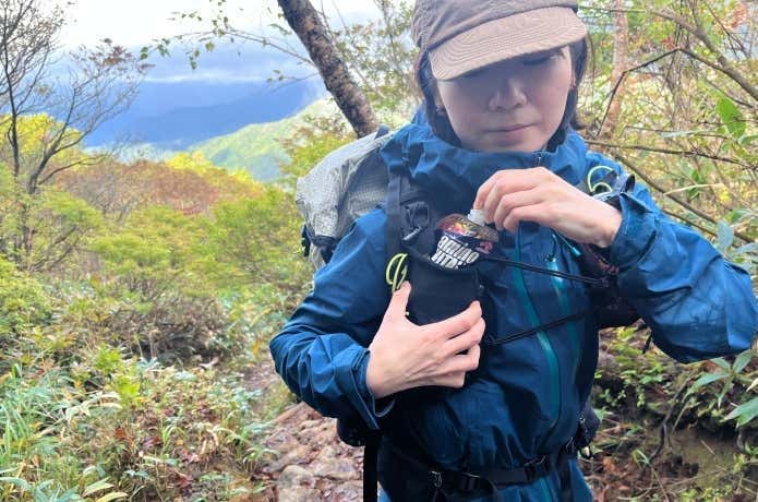 ショルダーハーネスのポケットから行動を出す登山者