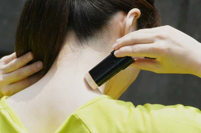 うなじ部分に日焼け止めスティックを縫っている女性