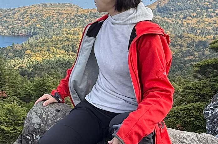 ワッフルウールフーディの上にシェルを着て岩に座る女性