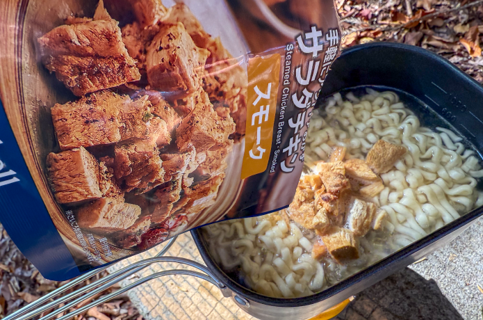 茹でたうどんにリゾッタサラダチキンを加える様子