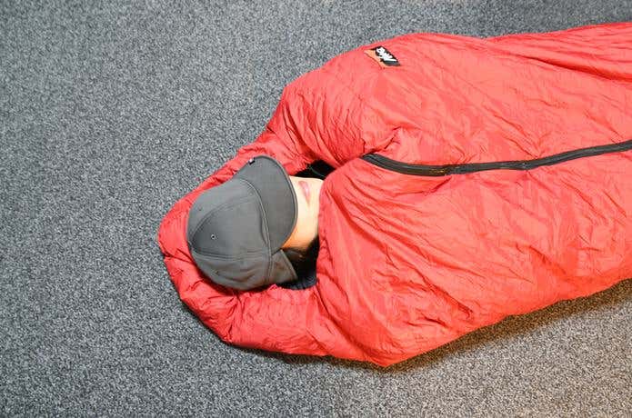 寝袋に入り、顔だけ出してカリマーのウォームイヤーカバーキャップをかぶって防寒する女性