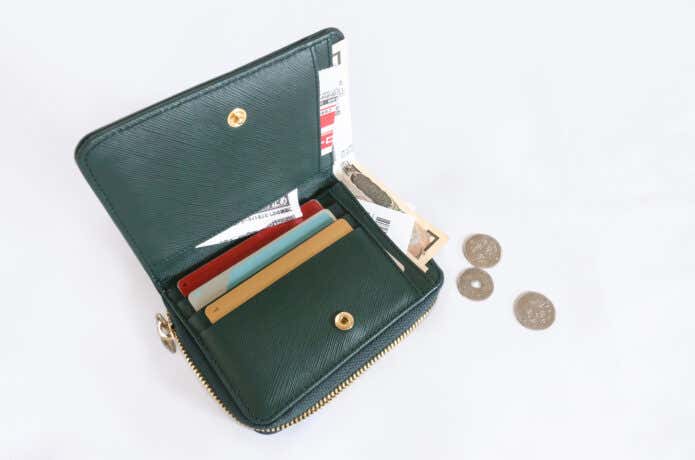 中身がごちゃごちゃした革の二つ折り財布。カードやお札が乱雑に入り、小銭がこぼれ落ちている様子。