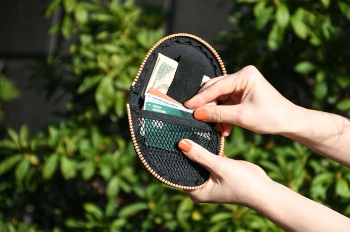 C&C.P.H.EQUIPEMENTのミニ財布を開いて、メッシュポケットにはカード類、ループ部分にお札をはさんでいる場面