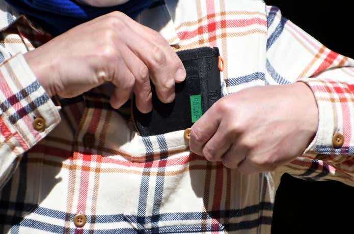 男性がC&C.P.H.EQUIPEMENTのミニ財布をシャツのポケットから取り出しているところ