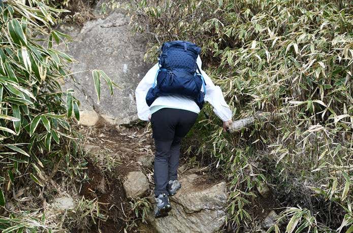 ユニクロ「ポケッタブルUVカットパーカ/NANODESIGN」を着て段差のある山道で体を大きく動かしている場面