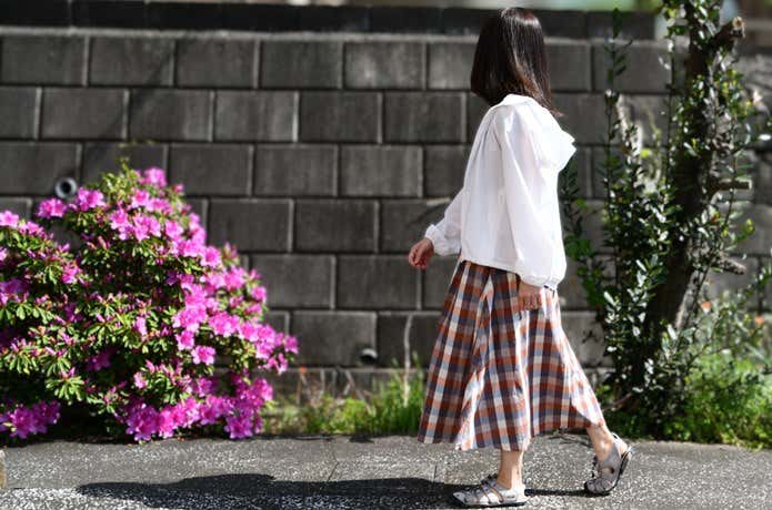 ユニクロ「ポケッタブルUVカットパーカ/NANODESIGN」を着て街を歩く女性。ツツジの花が咲く歩道で自然な着こなし