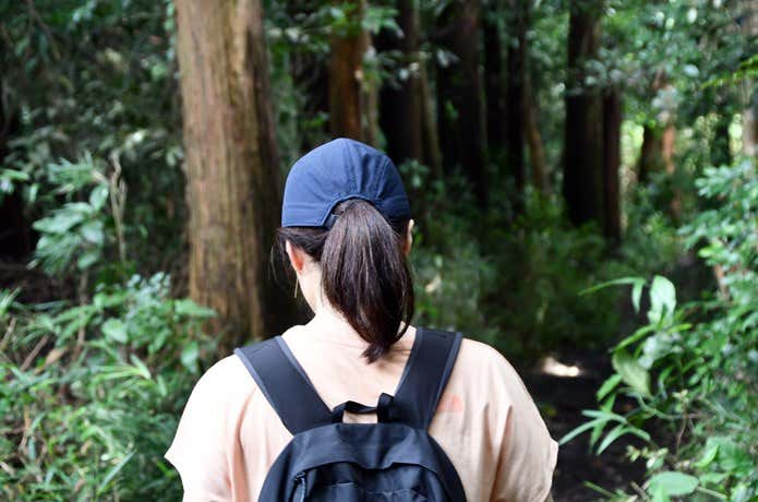 髪を一つに結び帽子をかぶったハイキング中の女性の後ろ姿