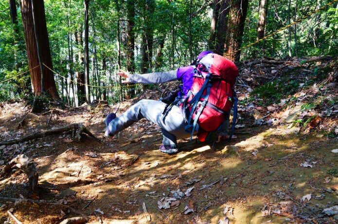 大きなザックを背負い、登山道で足を滑らせてバランスを崩す登山者